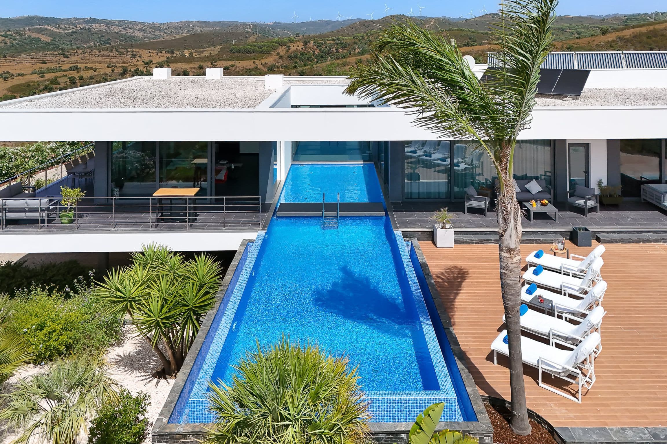Elevated view of the infinity pool passing beneath the villa's roof into an inner courtyard, with timber deck and loungers