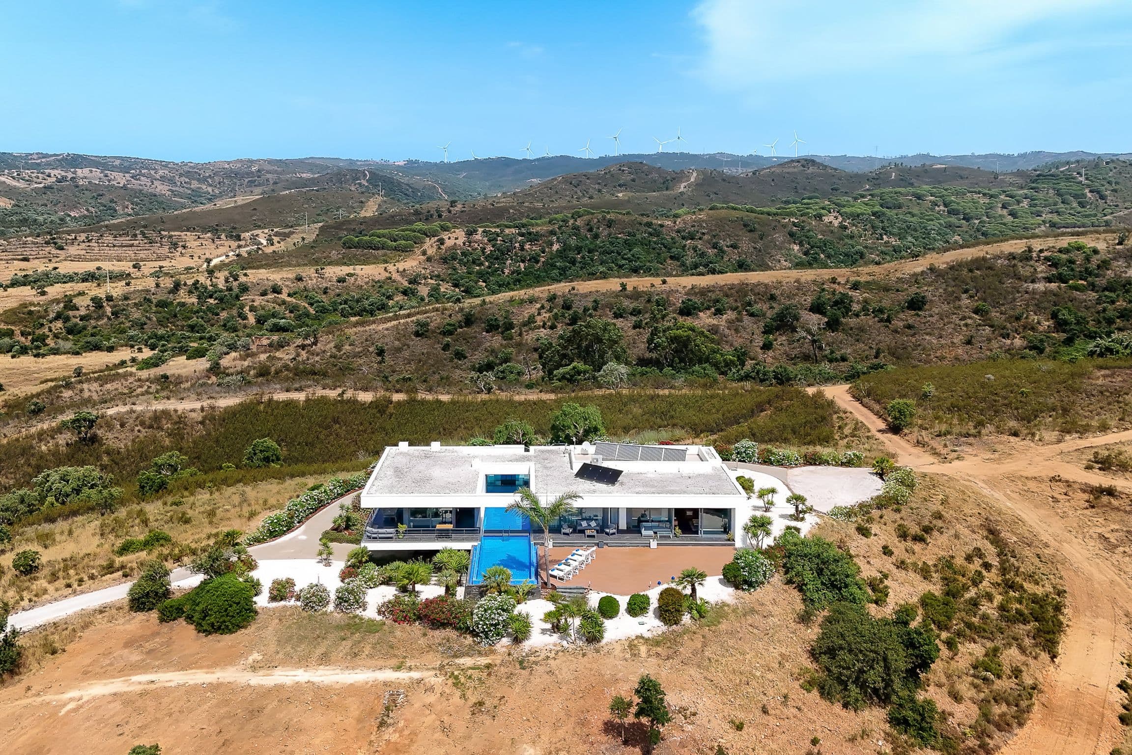 Aerial view of the white modernist villa alone on a hillside, rolling Algarve hills stretching to the horizon