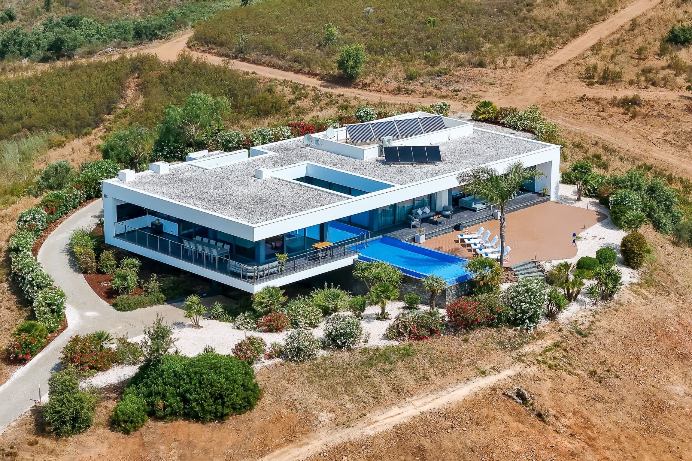 Aerial view of the villa with its flat roofs, courtyards, infinity pool and timber deck surrounded by planted gardens