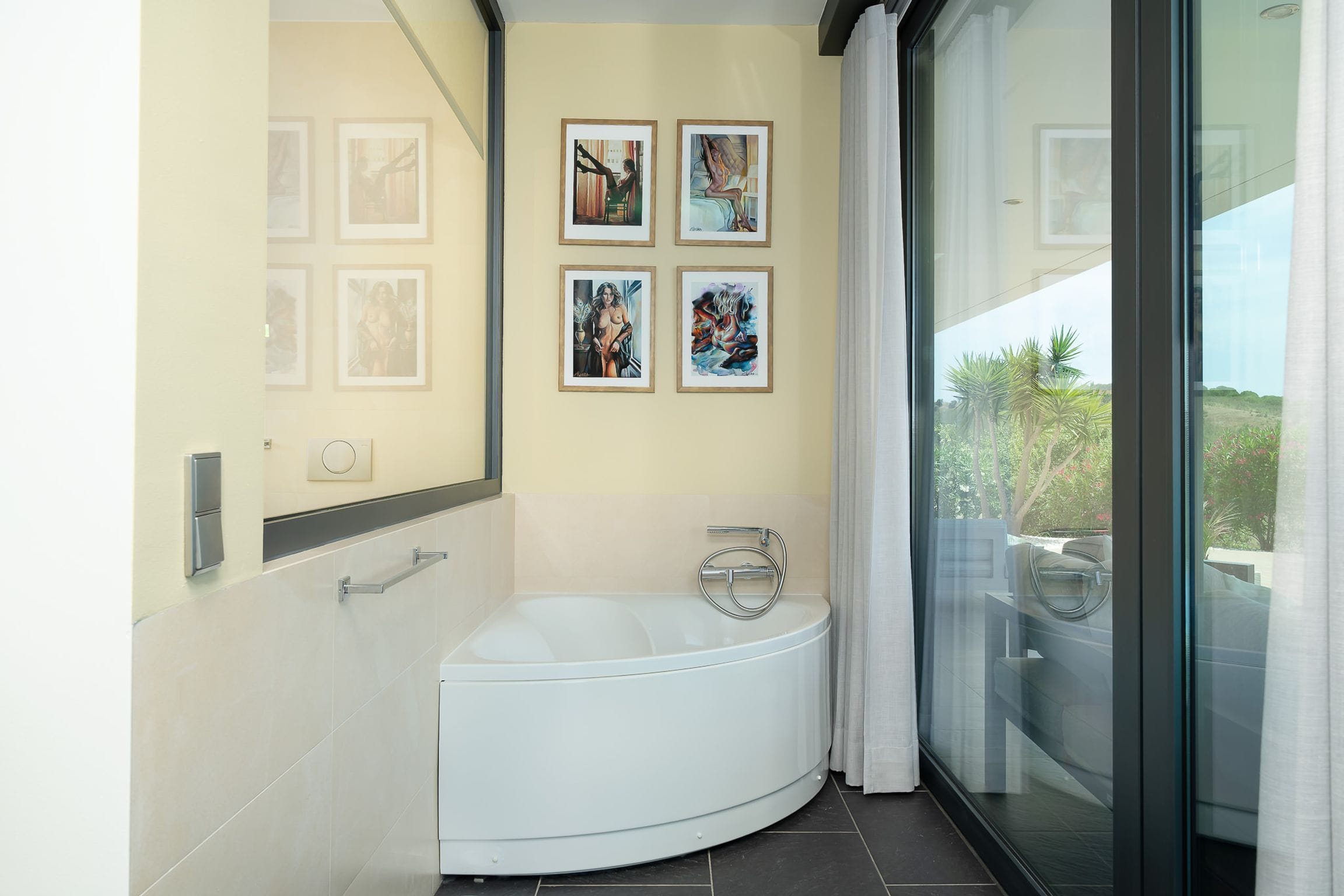 Corner bathtub beside full-height glass and sheer curtains