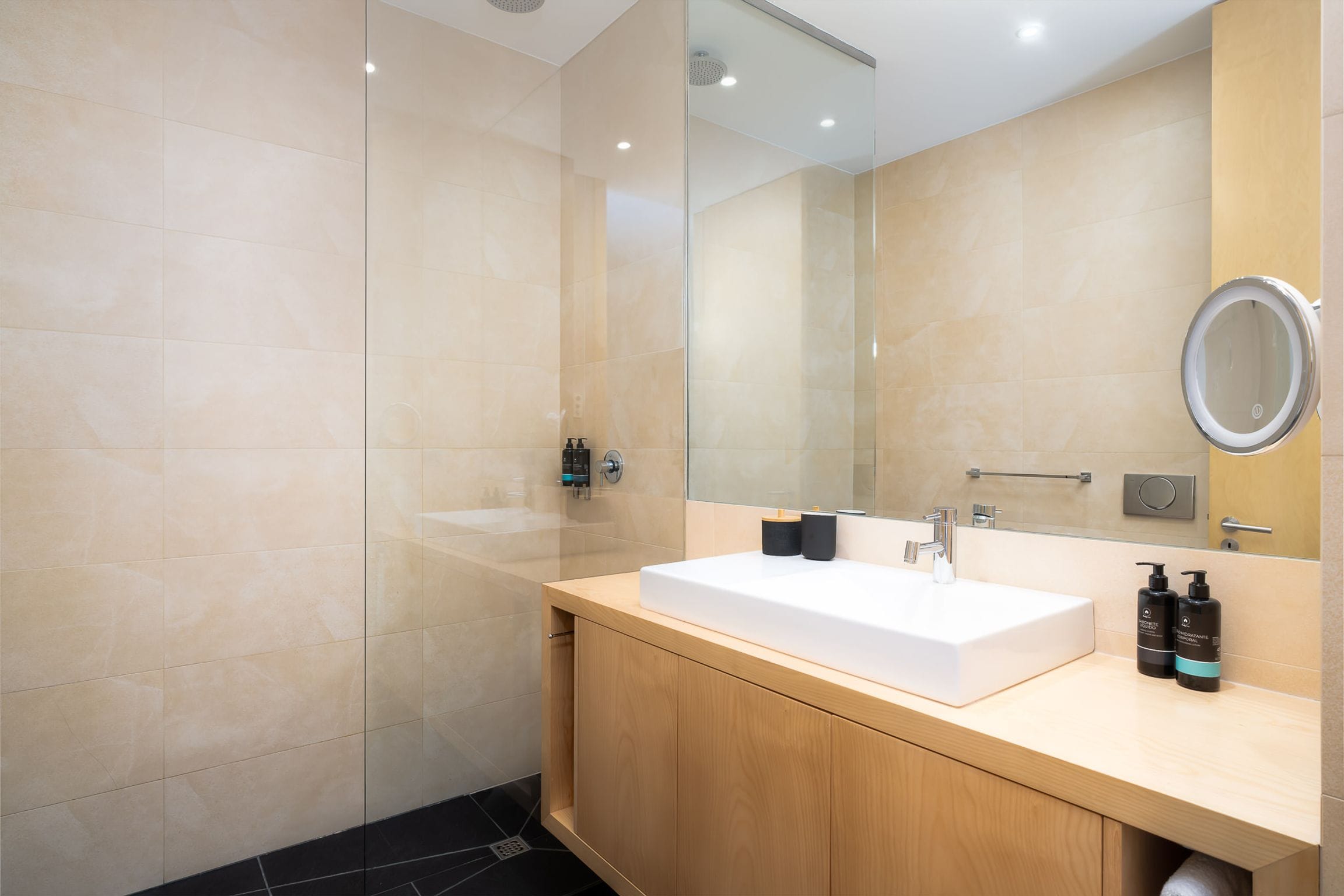 Bathroom in warm limestone tones with a frameless walk-in shower and timber vanity