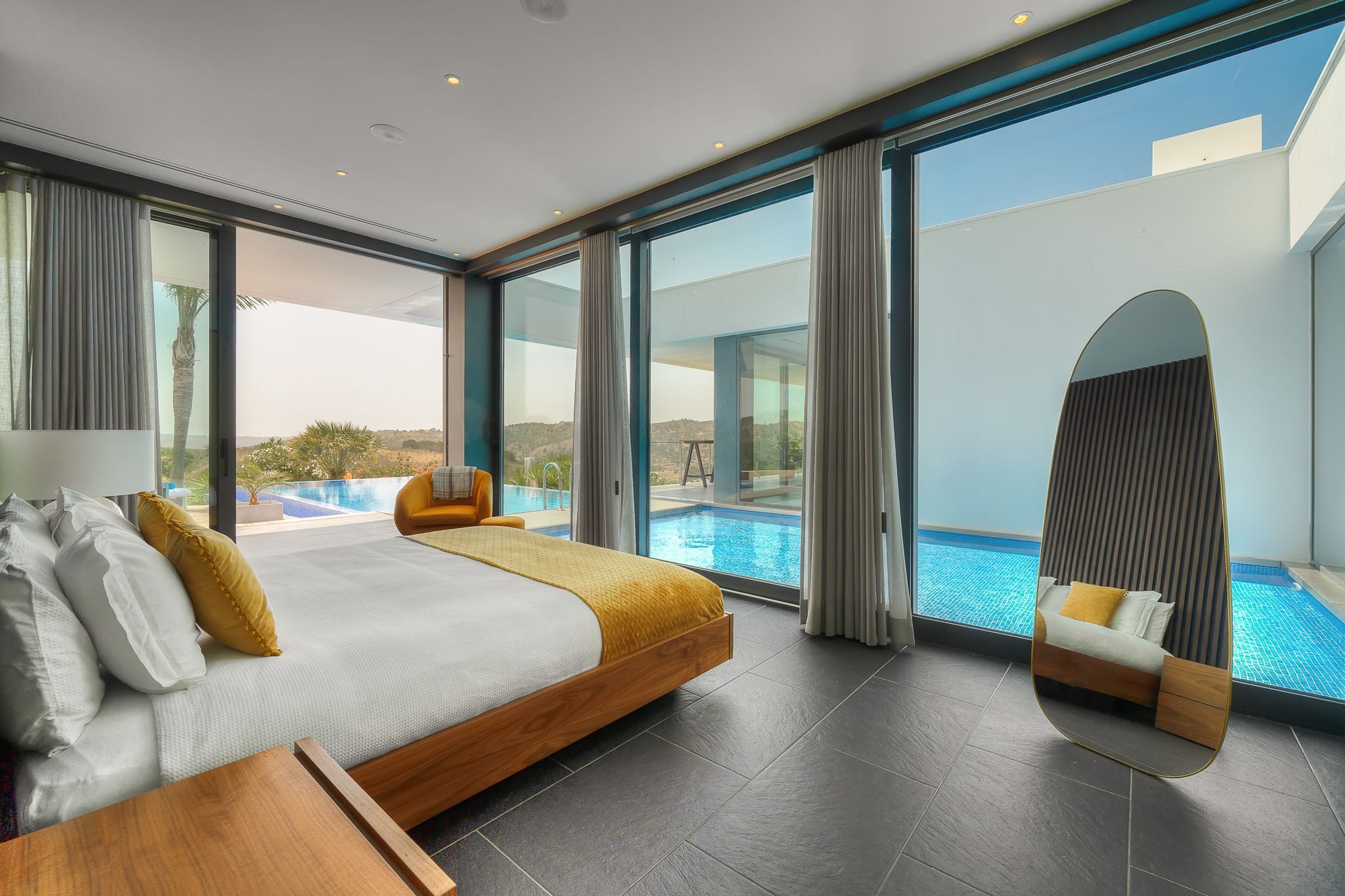 Bedroom with glass walls onto the courtyard pool, a sculptural mirror and garden views