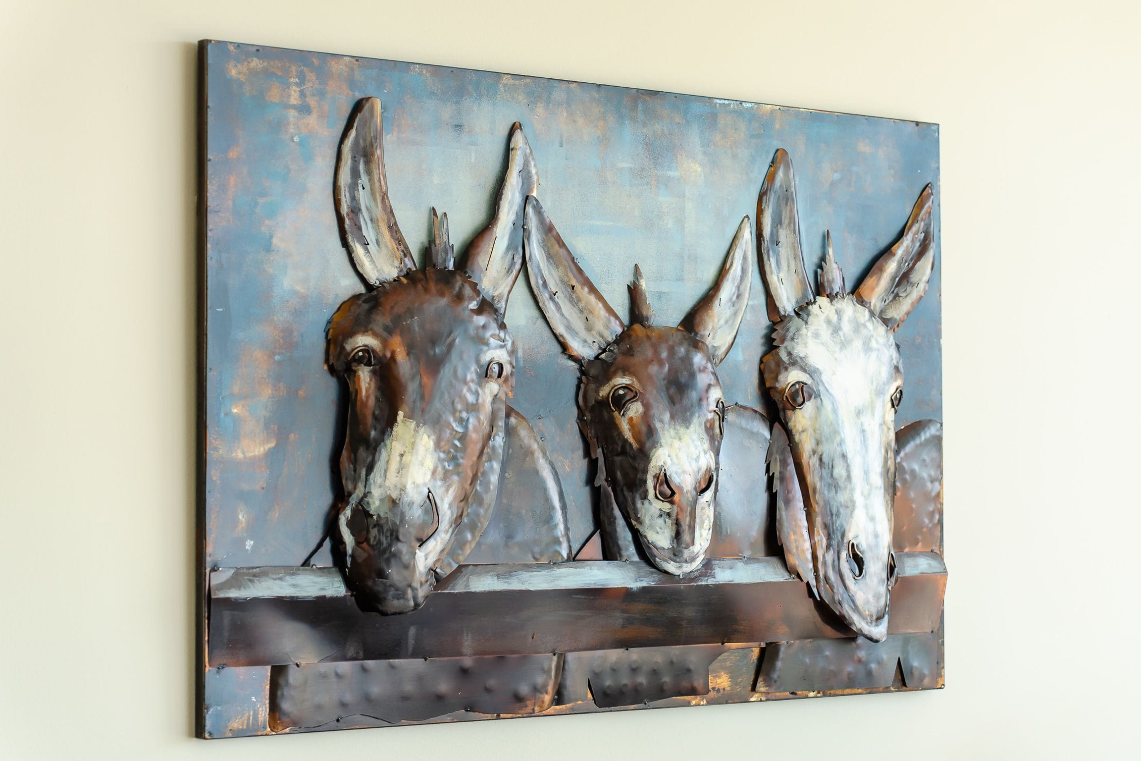 Textured metal artwork of three donkeys looking over a fence