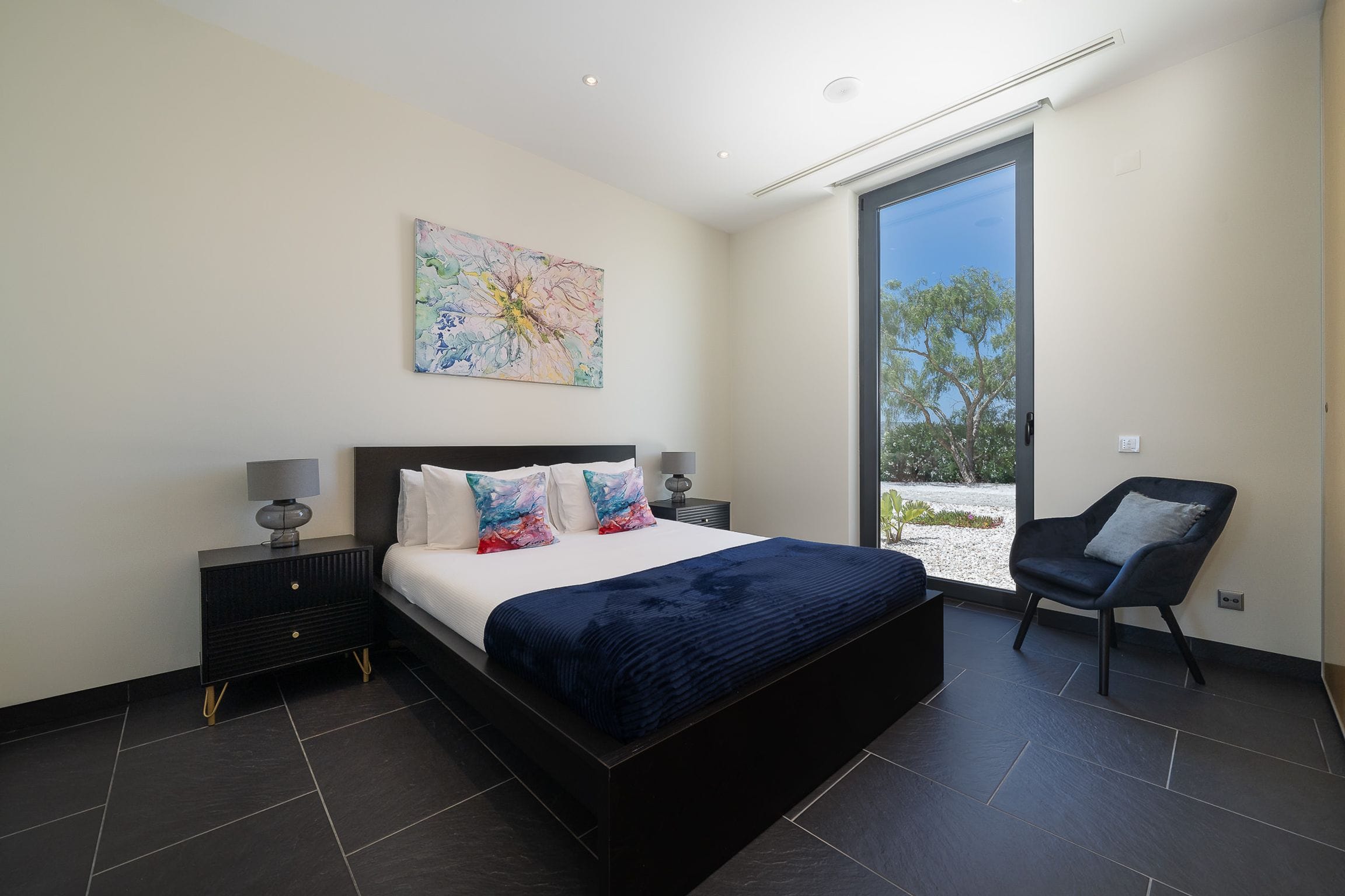 Double bedroom with a navy throw, abstract floral painting and tall window to the garden