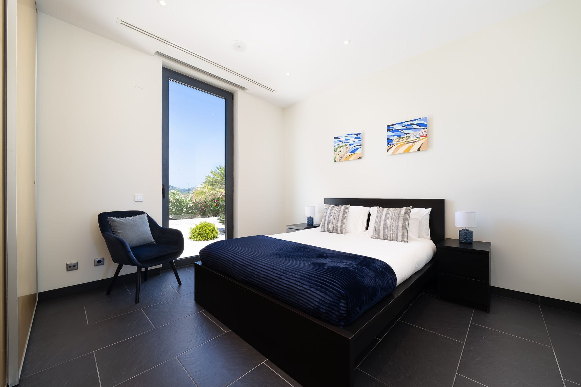 Double bedroom with navy bedding, a tall garden window and coastal artwork