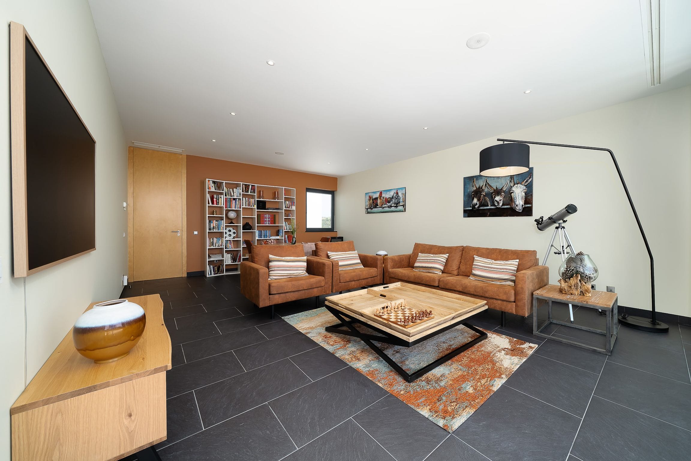 Relaxed lounge with tan leather sofas, a timber games table, bookshelves and a telescope