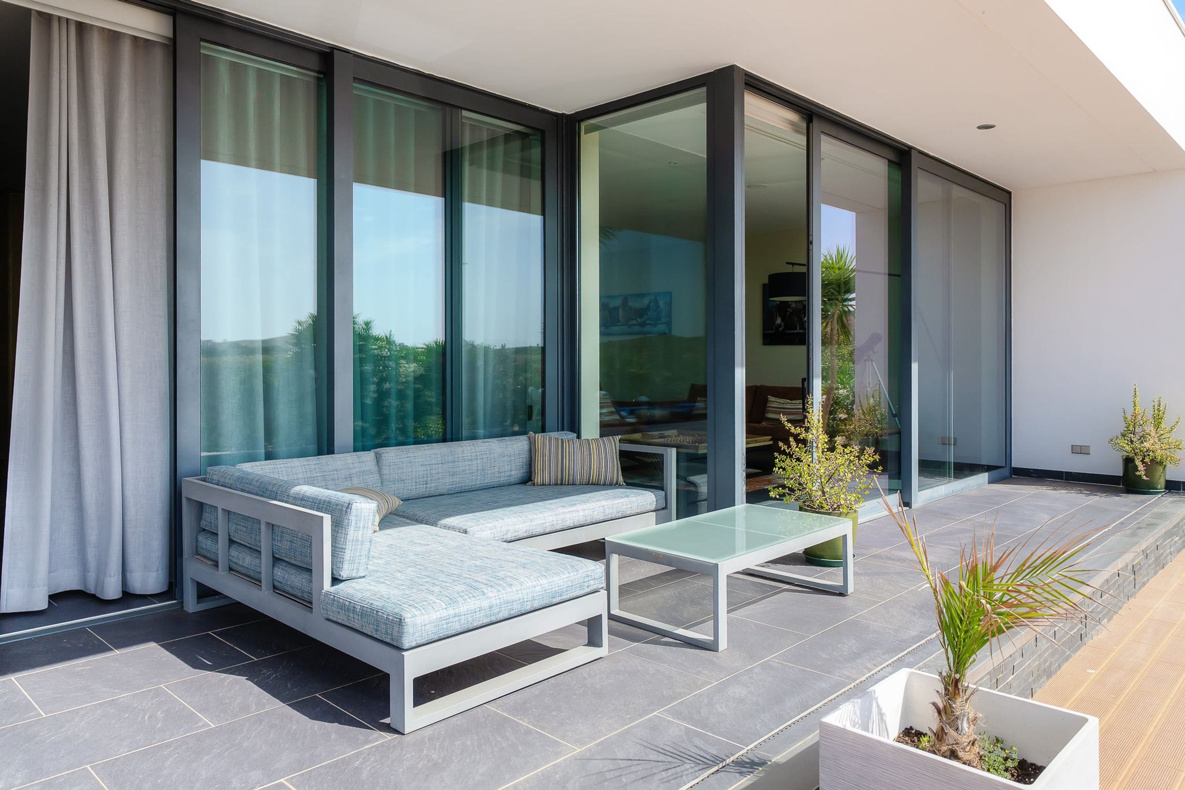 Corner sofa on the terrace beside open floor-to-ceiling glass doors