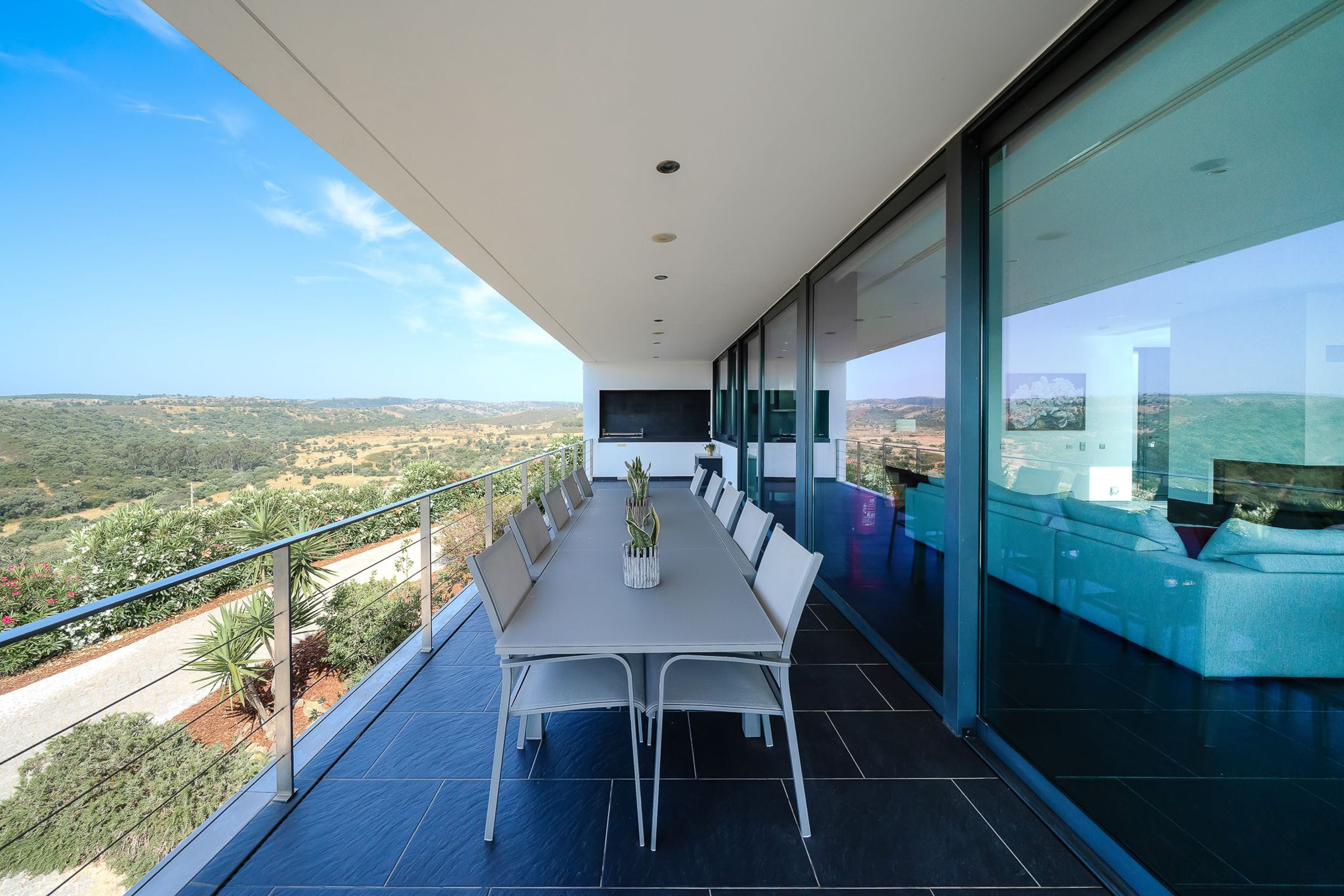 Long outdoor dining table running along the glass facade of the upper terrace towards the view