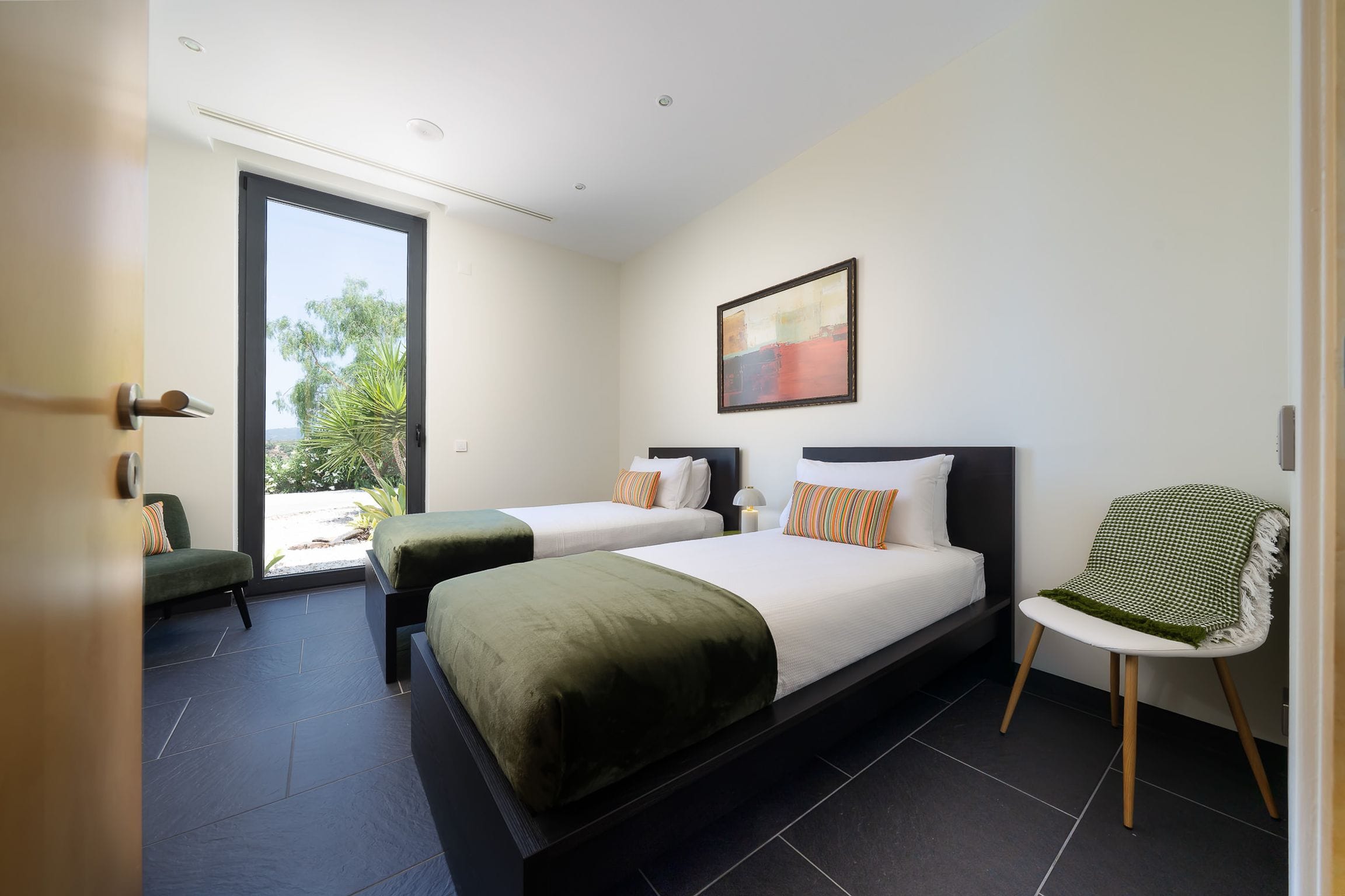 Twin bedroom with olive-green throws and a tall glass door onto the garden